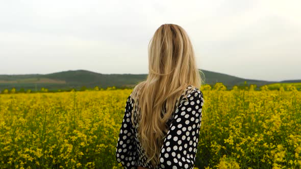 Blond woman walking in field of yellow rapeseed, handheld slow motion