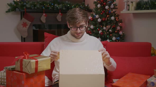 Young man is opening a gift box, light shines on face.