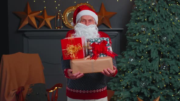 Senior Grandfather Parodies Santa Claus Presenting Christmas Gift Box Holidays Celebration at Home