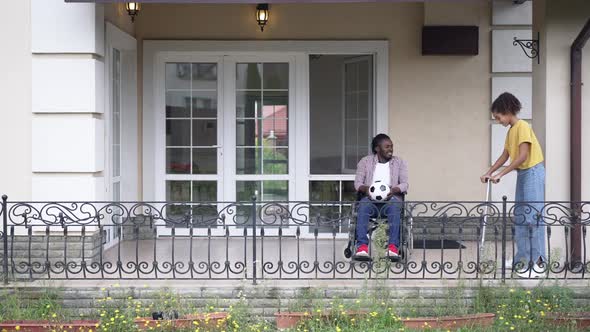 Wide Shot African American Man in Wheelchair Sitting on Porch with Soccer Ball As Teenage Girl