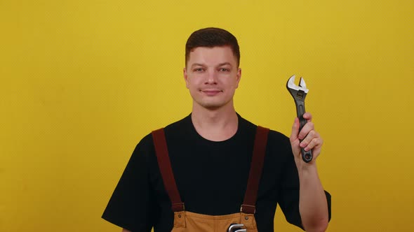 A Young Plumber in Work Clothes Holds Tools in His Hands on a Yellow Background