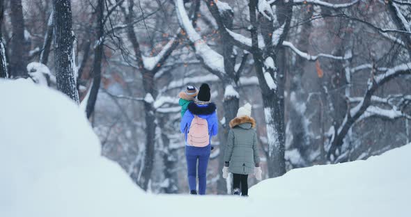 Young Woman Walks Along a Snowy Road in a Winter Forest with Children