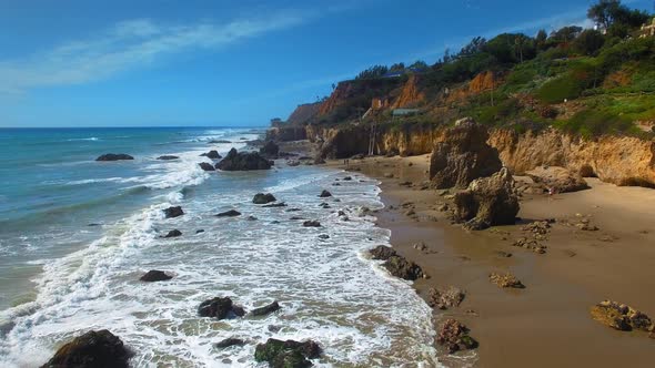 Aerial camera moving over rocks and foaming waves at El Matador Beach Malibu, Califronia, USA