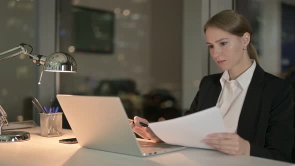 Businesswoman Working on Document and Laptop in Office at Night 