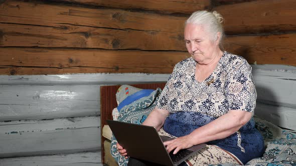 Elderly Woman with Gray Hair Holds a Laptop on Her Lap Sitting on a Bed