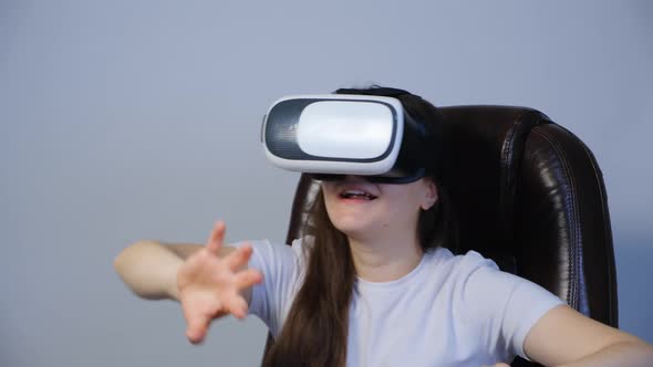 A Woman with Vitrual Reality Glasses Sits in a Chair and Moves Her Hands Around