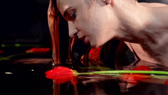 Elegant Portrait of a Girl with a Long Neck Lying in the Water with Red Tulip Flowers