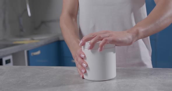 Female Hand Grabs White Jar and Unscrews Lid on It