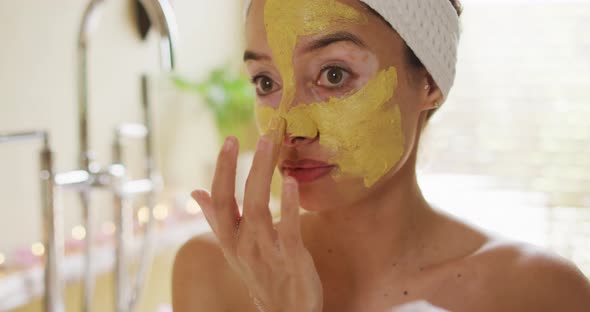 Portrait of biracial woman looking into mirror and applying face mask