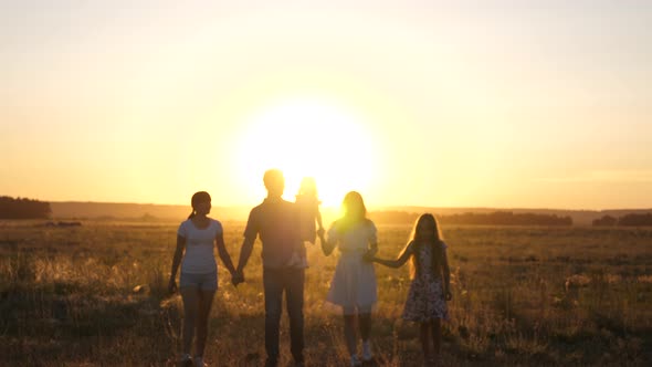 Happy Family Walks in Field in Sunset Light. Dad Mom and Daughters Are Walking in Park in the Light