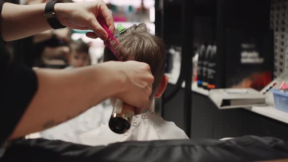 Fashionable Hairdresser Cuts a Child's Hair with a Clipper in a Barbershop