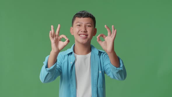 A Portrait Of A Happy Young Asian Boy Showing Okay Gesture To The Camera In The Green Screen Studio
