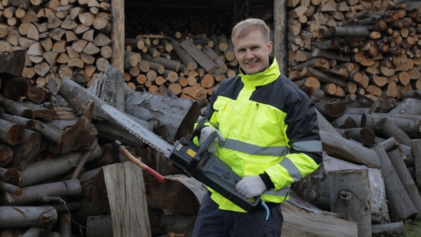 Lumberjack in Reflective Jacket. Man Woodcutter with Electric Chainsaw. Sawn Logs, Firewood, Sawmill