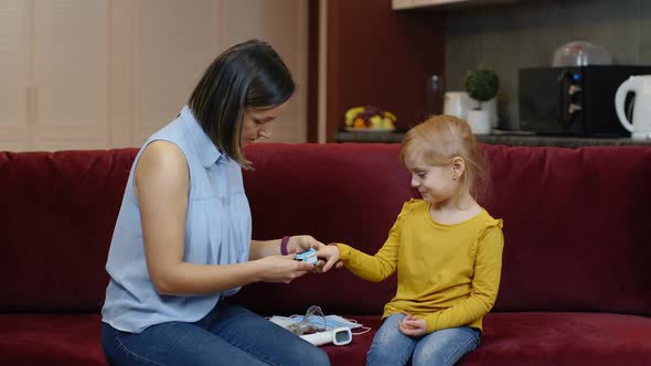 Mother Measuring, Monitoring Oxygen Saturation with Digital Pulse Oximeter of Her Daughter at Home