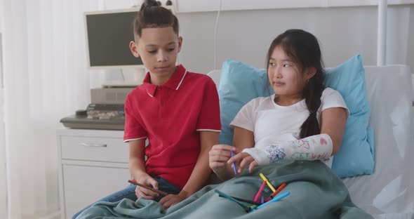 Mixedrace Preteen Boy Visiting Asian Girl Friend in Hospital Painting Hand Cast Together