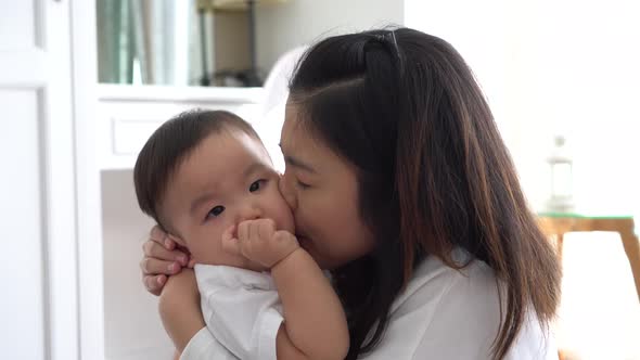 Asian Young Adult Mother Kissing Joyful Son in Living Room