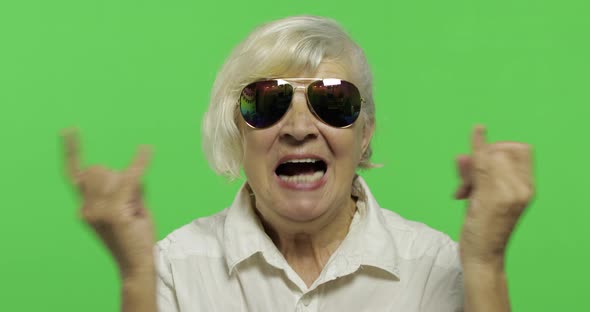 An Elderly Woman Show Sign of the Horns with Her Hands and Showing Tongue