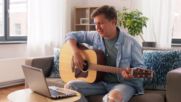 Young Man with Laptop Playing Guitar at Home