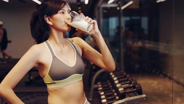 Attractive fitness asian woman finishing workout and drinking protein milk shake