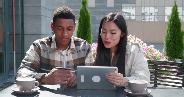 Happy Couple of African Man Holding a Credit Card and Cheerful Asian Woman with Tabletsitting at the