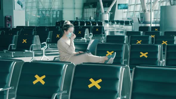 A Lady in a Face Mask is Using a Laptop Among Marked Airport Seats