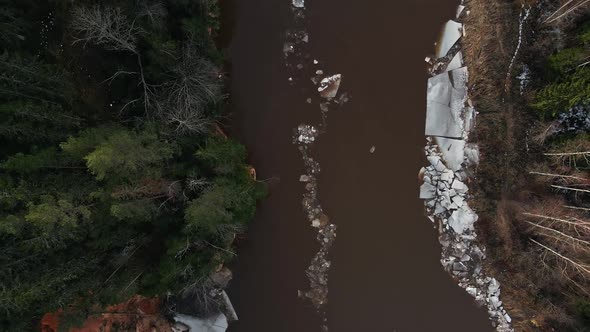 Top Down Ice Flows Along River Surrounded By Forest and Cliffs in Spring Aerial