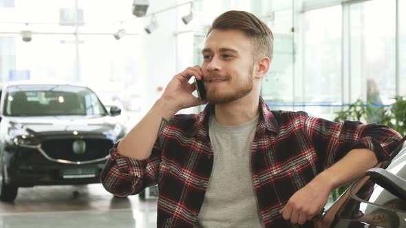 Cheerful Handsome Man Talking on the Phone at the Car Dealership