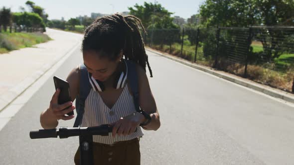 African american woman on scooter using smartphone and smiling