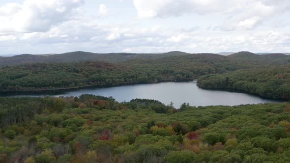 Pull back aerial view of a calm lake in a dense forest in autumn