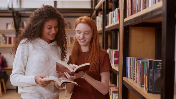 Young Beautiful Girl with Curly Hair and White Sweater Discussing Books with Female Redhead Teenage