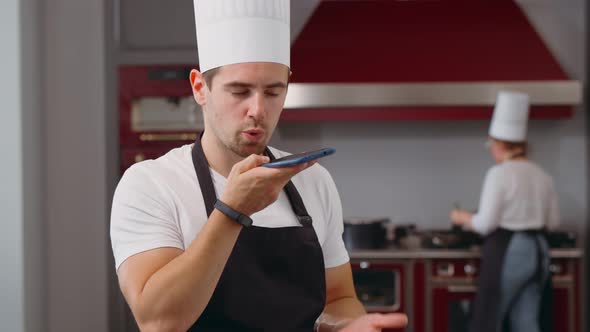 Male Chef Cook Recording Voice Message on Smartphone at Restaurant Kitchen