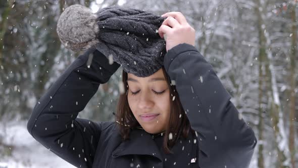 Beautiful female putting on winter hat during heavy snowfall