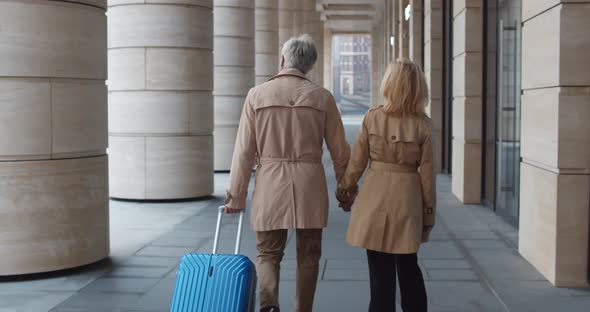 Follow Shot of Mature Tourist Couple Carrying Suitcase Walking Outdoors