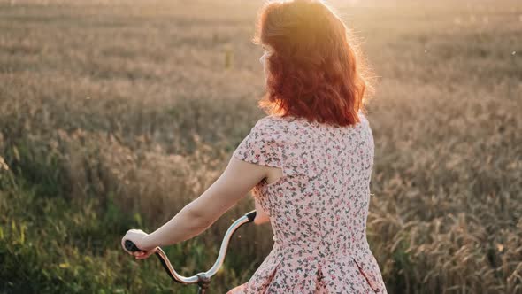 A Girl on a Bicycle is Riding a Field Road at Sunset