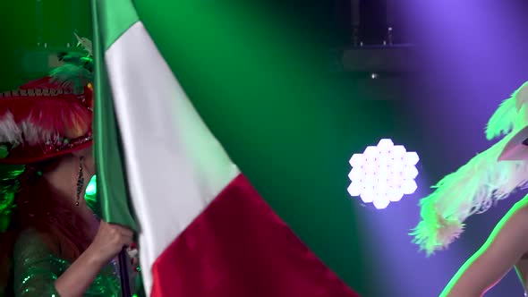 Sexy Woman in Green Shiny Suit Is Dancing with the Italian Flag Against the Background of Colored