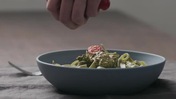 Slow Motion Man Hand Add Cherry Tomatoes to Green Fettuccine with Pesto in Blue Bowl