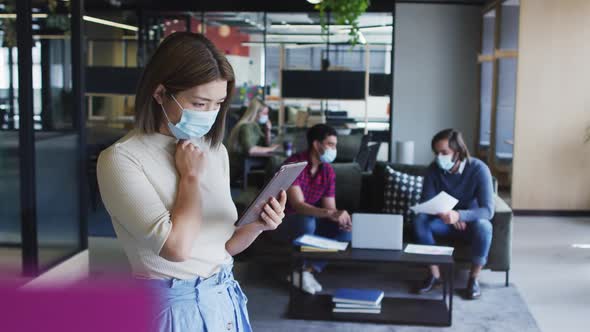 Asian businesswoman wearing face mask using digital tablet modern office