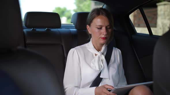 Serious Woman Using Tablet Going To Work By Taxi