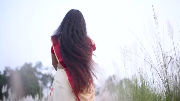 An Indian woman in saree with beautiful long and curly hair sways and moves her hair in a field, slo