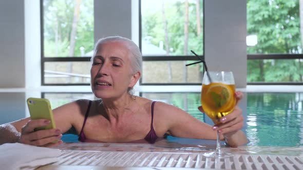 Aging Woman with Phone and Cocktail Drink in Pool