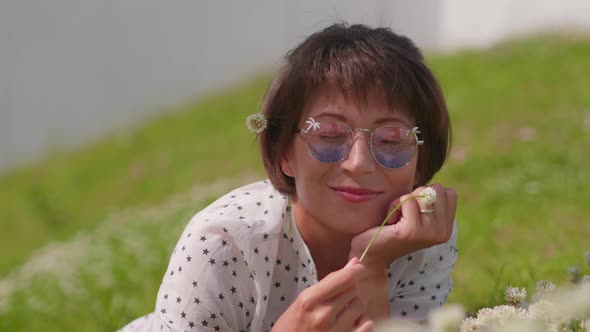Woman with Colorful Sunglasses Lays on Lawn in Urban Park and Enjoys Flowers