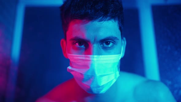 Portrait Serious Man in a Medical Mask Looks at the Camera in Neon Lighting