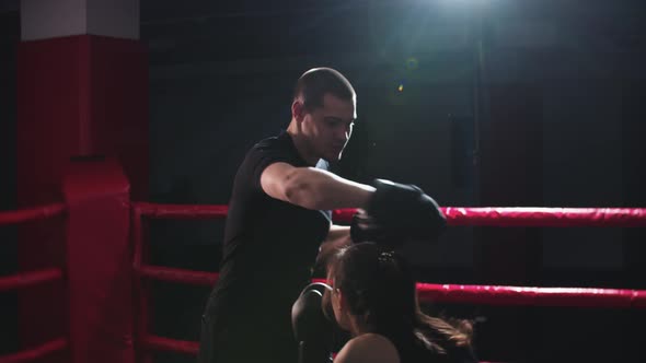 Young Woman with Long Hair Training Boxing with Her Personal Trainer on the Ring in the Dark