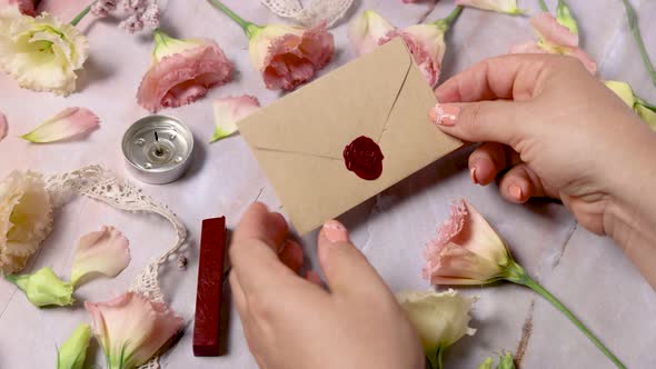 Hands taking wax sealed envelope from a marble table near pink flowers