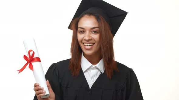 Smiling Attractive Female African American Graduate in Academic Dress Holding Her Diploma and