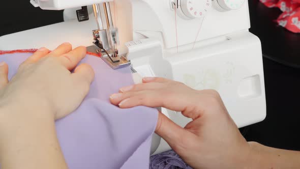 woman's hands sew the edge of fabric on sewing machine