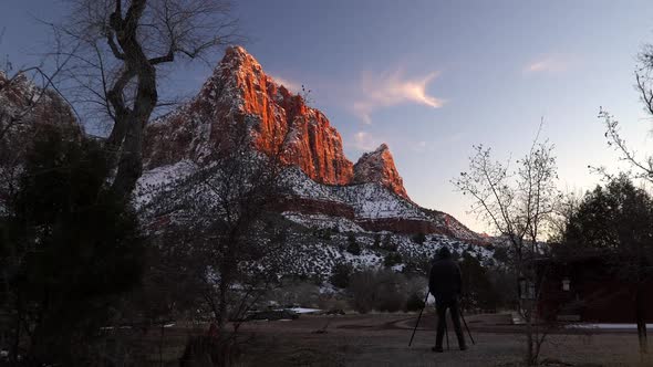 Walking up behind man photographing cliff glowing in Zion during winter