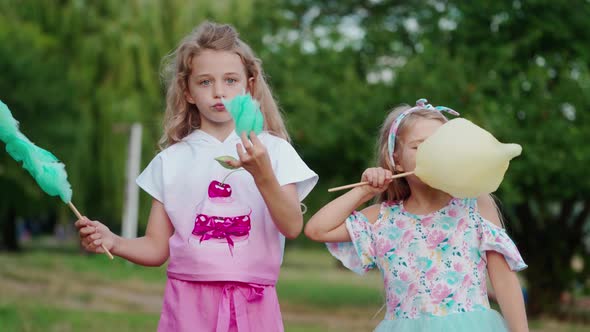 Two little girls eating cotton candies outdoors
