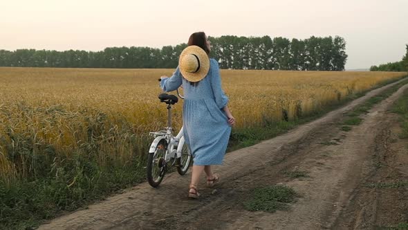 Woman walks along rural road wheat field on bike enjoying life and nature