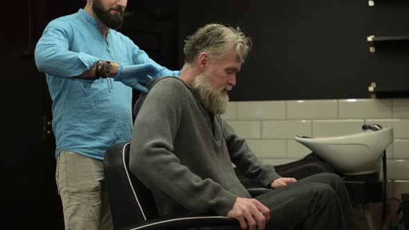 A gray-haired man sits in a barber's chair and expects a haircut